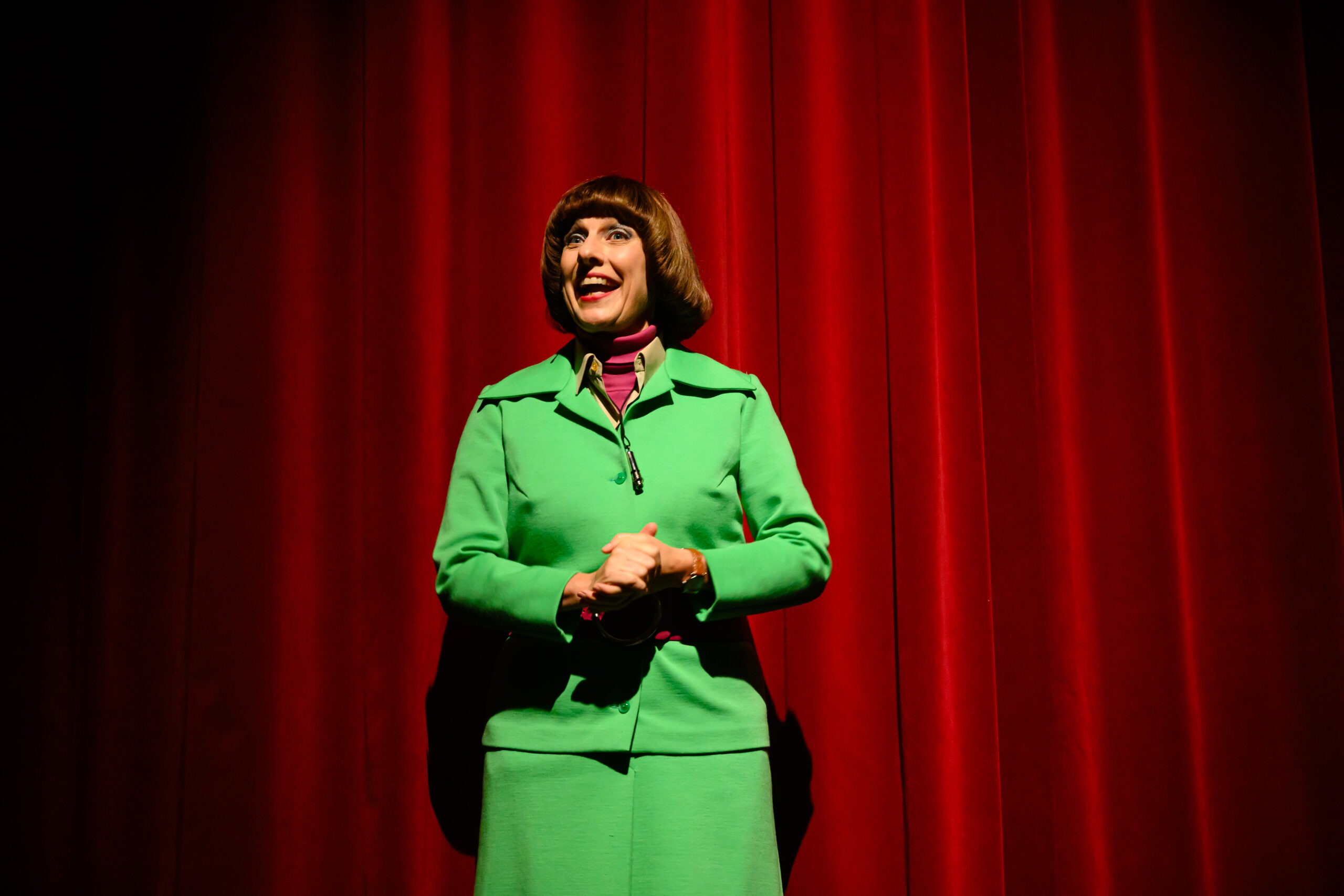 Vrouw met groen mantelpakje staat voor een rood theatergordijn