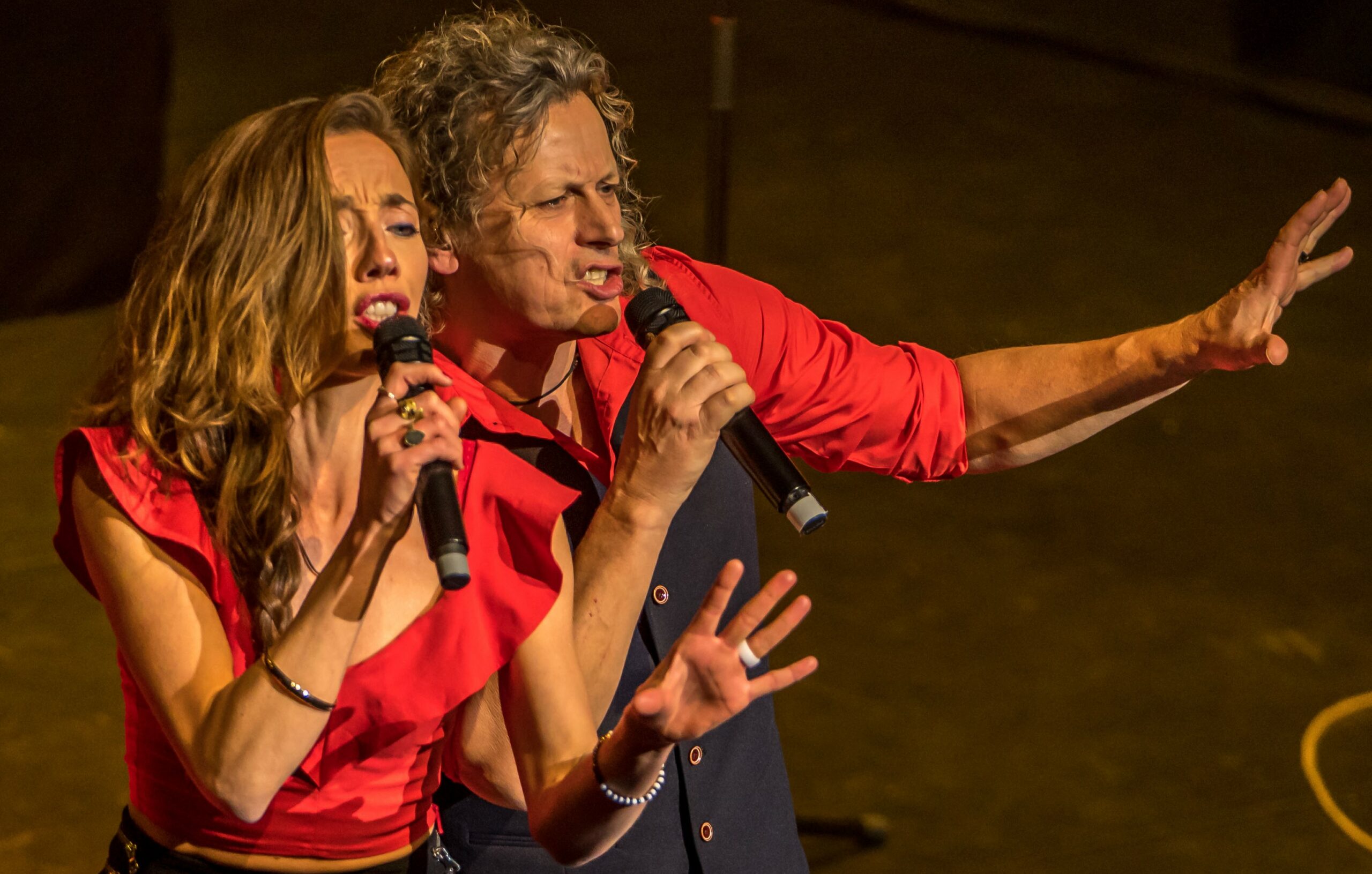 Zanger en zangeres gekleed in het rood zingen in een microfoon