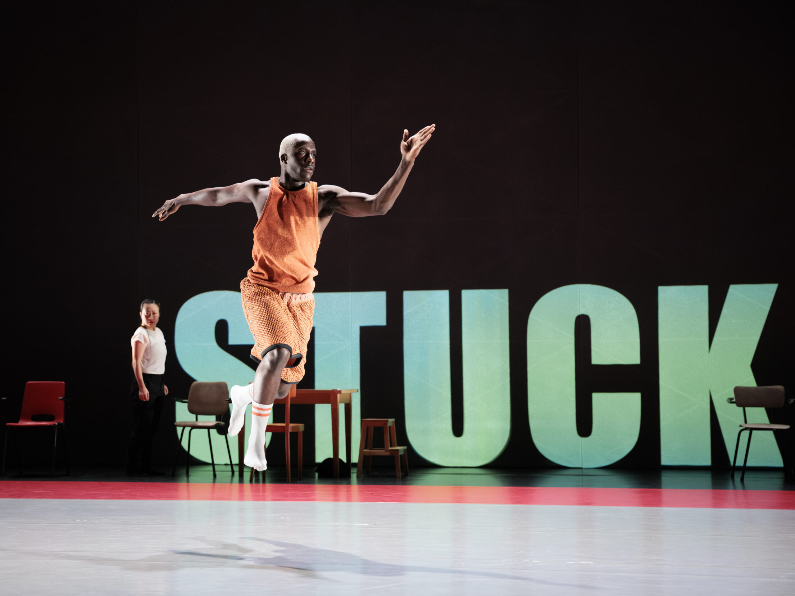 Een danser die met zijn armen wijd over het podium springt met het woord 'stuck' op de achtergrond