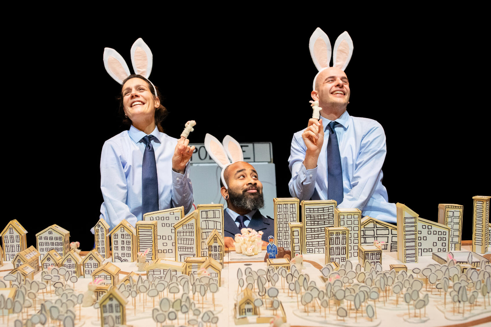 Drie agenten met konijnenoren en konijnen vingerpoppetjes kijken over een plattegrond uit van een stad
